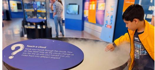 A student reaching into a cloud exhibit at a science visitor center