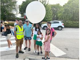 A group of students and adults outdoors next to a large white weather balloon