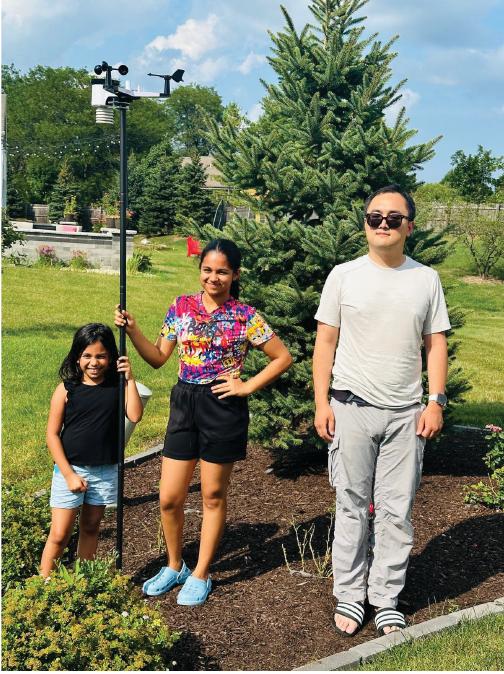 Three people standing beside a newly installed backyard weather station